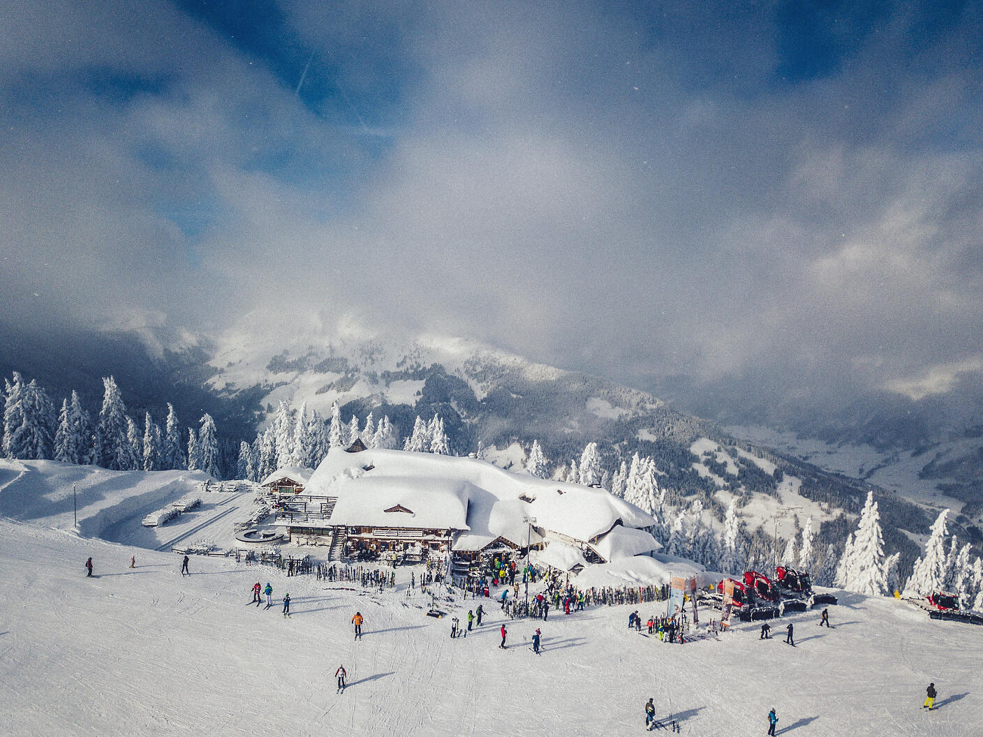 Eingebettet in eine atemberaubende Bergkulisse präsentiert sich der Krallerhof als winterliches Skiparadies. Verschneite Tannen rahmen die Skistation ein, während zahlreiche Wintersportler über die glitzernde Piste gleiten und die majestätische Berglandschaft des Salzburger Landes genießen. Verschneite Winterlandschaft mit Skistation und Bergpanorama. Zahlreiche Skifahrer vor verschneiten Gebäuden und winterlich weißen Tannen.