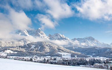 Die Winterlandschaft von Saalfelden Leogang entfaltet sich in atemberaubender Pracht: Mächtige, von Schnee bedeckte Berggipfel erheben sich über einem sanft verschneiten Tal. Tannen und Fichten tragen eine weiße Winterrobe, während vereinzelte Gebäude friedlich in der klaren, eisigen Bergluft ruhen. Die Szenerie strahlt eine unbeschreibliche Ruhe und alpine Erhabenheit aus. Winterliche Berglandschaft mit verschneiten Gipfeln und einer malerischen Talansicht. Verschneite Wälder und Siedlungen im Vordergrund, dramatische Alpenkulisse im Hintergrund.
