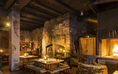Rustic dining room with stone walls and open fireplace, cozily lit with wooden furniture and historic ambiance.