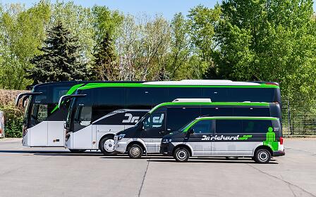 Three travel buses from the Dr. Richard Group parked on an asphalt parking lot, surrounded by green trees and vegetation.