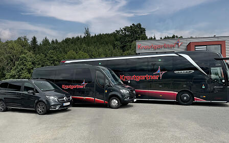 Die vielseitige Krautgartner-Flotte vereint Reisebus und komfortable Vans vor dem Firmengebäude. Einheitliches Branding, modernes Design und großzügige Ausstattung stehen für flexible Mobilitätslösungen, exzellenten Service und professionelle Personenbeförderung.