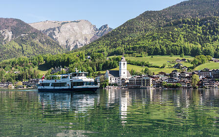 Idyllic lake landscape with white boats at the shore of St. Wolfgang, surrounded by lush green mountain slopes and traditional alpine architecture.