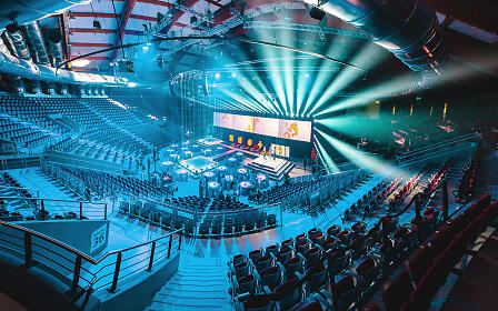 Eine eindrucksvolle Arena im Messezentrum Salzburg entfaltet sich in kühlem Blau: konzentrische Sitzreihen umrahmen eine zentral platzierte Bühne, während präzise Lichtstrahlen die Szene durchziehen und eine hochmoderne Eventatmosphäre schaffen.