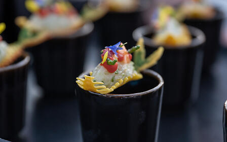 Kunstvoll dekoriertes Fingerfood in schwarzen Bechern mit Blüten und feinen Zutaten.