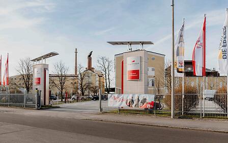 The entrance to a large brewery site features flags, modern gate structures and historic buildings. The combination of industrial architecture and brand presentation highlights the connection between brewing tradition and modern beer production.