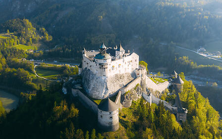 The majestic Hohenwerfen Fortress stands atop a rocky spur, surrounded by forested alpine hills.