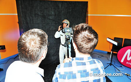 Two people stand in front of the camera during the supporting programme film shoot and film another person wearing a helmet and standing in front of a black screen.