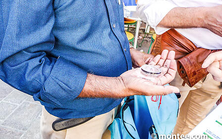 Two hands exchanging a small glass container, one wearing a blue shirt, the other a white blouse.