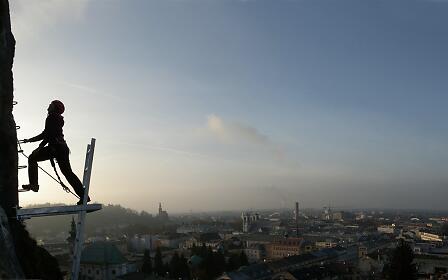 Silhouette of a climber on scaffolding overlooking the cityscape of Salzburg during sunrise or sunset.