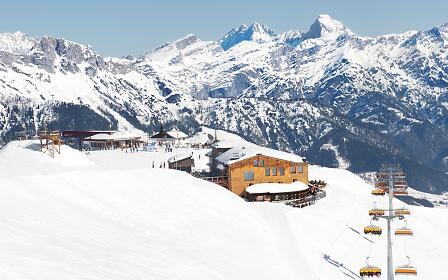 Snowy mountain landscape with ski resort, orange mountain restaurant, and chairlift against impressive mountain backdrop with snow-covered peaks.