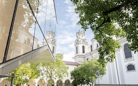 Modern architecture reflects the baroque façade of the university church. Glass, light, and history merge in the heart of Salzburg.