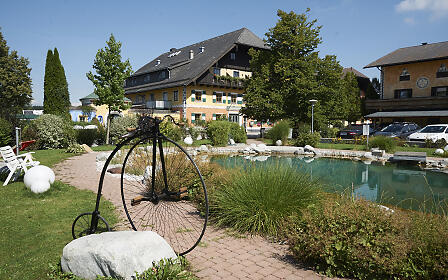 Idyllic garden with pond and vintage high-wheel bicycle in front of the traditional country inn Gastaghof with yellow facade and balcony.