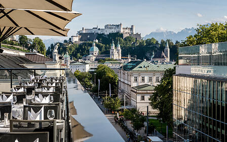 Die stilvoll gedeckte Dachterrasse eröffnet einen atemberaubenden Blick auf Salzburgs Altstadt, den Dom und die Festung Hohensalzburg – ein exklusiver Ort für kulinarische Genüsse über den Dächern der Stadt.