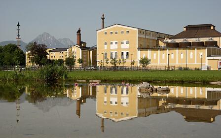 The iconic Stiegl brewery reflects in a tranquil pond, with Mount Untersberg in the background – a picturesque blend of nature and tradition.
