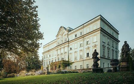 Schlossfassade mit Skulpturen und spätsommerlichem Garten