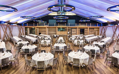 Festlich gedeckter Veranstaltungsraum mit weißen Tischen, grauen Samtsessel und blau-violetter Deckenbeleuchtung in der Festalm Bad Hofgastein.