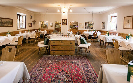 Gasthof Schloss Aigen combines rural elegance with classic charm. Wooden floors, simple farmhouse chairs, and lovingly set tables with white cloth napkins create a warm, traditional atmosphere in a historic setting. Dining room at Gasthof Schloss Aigen with wooden furniture, carpet, and classically set tables.