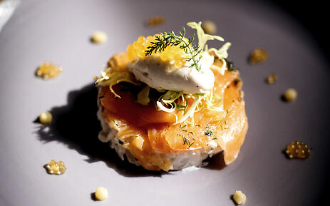 At Restaurant Blaue Gans, house-cured salmon is artfully presented: on a delicate bed of rice, topped with frisée, cream, and dill. Surrounded by decorative drops, the interplay of light and shadow gives the dish a refined stage. Salmon dish at Restaurant Blaue Gans on rice with cream, dill, and delicate garnish.