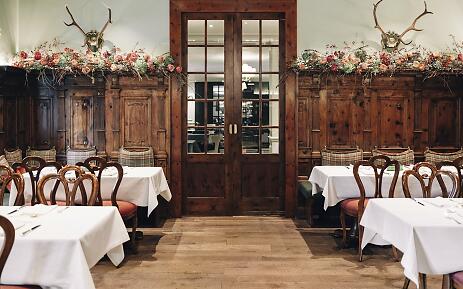The Zirbelzimmer at Hotel Sacher Salzburg enchants with richly carved wood paneling, elegant antlers, and floral décor. White tablecloths and checkered seat cushions add traditional charm and an exclusive sense of comfort. Zirbelzimmer at Hotel Sacher Salzburg with wood paneling, flowers, and stylish coziness.