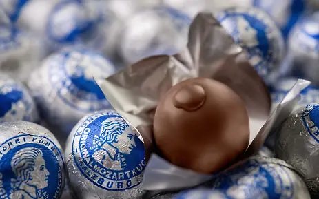Mozartkugeln in blau-silbernen Verpackungen, eine Schokoladenkugel im Zentrum, typisches Salzburger Süßwarenensemble.