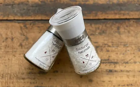 Zwei weiße Salzstreuer mit minimalistischem Design auf einer rustikalen Holzoberfläche, gefüllt mit feinem weißem Salz.