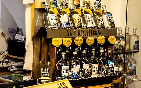 Gin-Regal mit verschiedenen Flaschen und Auszeichnungen in einer Destillerie, präsentiert auf Holzregalen mit gelben Markierungen.