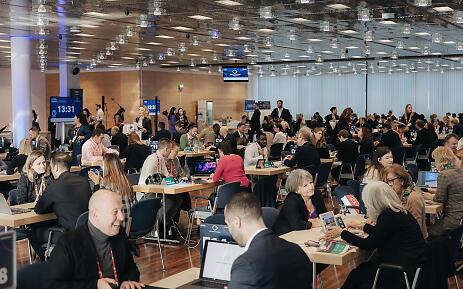 Ein pulsierender Treffpunkt der Kommunikation: Der Konferenzsaal ist erfüllt von konzentrierter Geschäftigkeit. Elegante Holztische, hochmoderne Technik und eine atmosphärische Beleuchtung schaffen eine professionelle Arbeitsumgebung, in der Ideen ausgetauscht und Strategien entwickelt werden. Großer Konferenzsaal mit zahlreichen Teilnehmern an Tischen, ausgestattet mit Laptops und Bildschirmen unter einer modernen Deckenbeleuchtung.