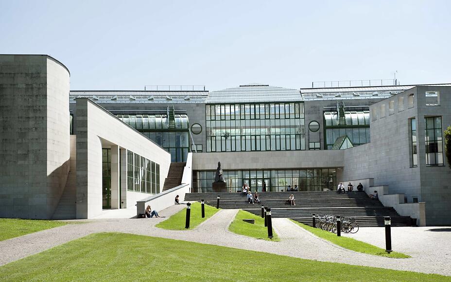 Modern concrete building with glass facades, open stairs, and green areas. Contemporary architecture with clean lines and an inviting entrance.