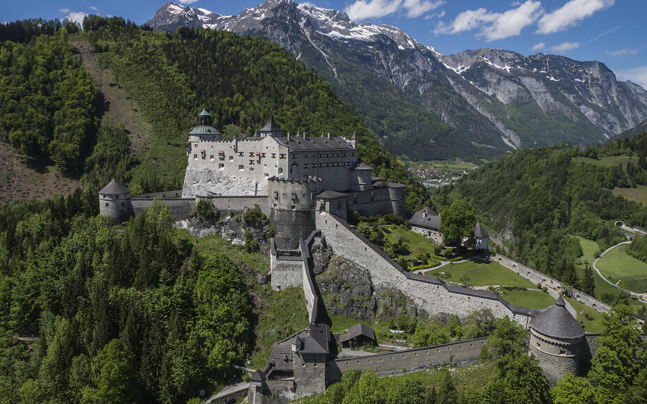 Mittelalterliche Festung Hohenwerfen thront auf felsigem Bergvorsprung, umgeben von dichten Wäldern und majestätischen Alpengipfeln mit Schnee.
