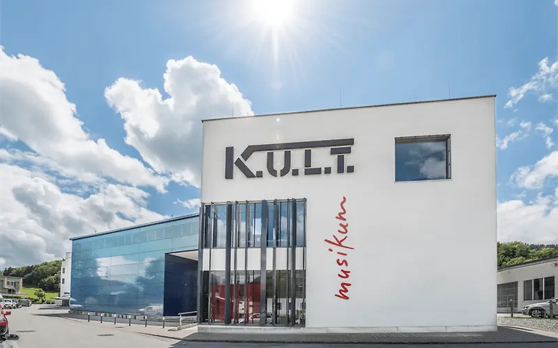 Modern white office building with blue glass facade on a sunny day, K.U.L.T. company logo on white wall.