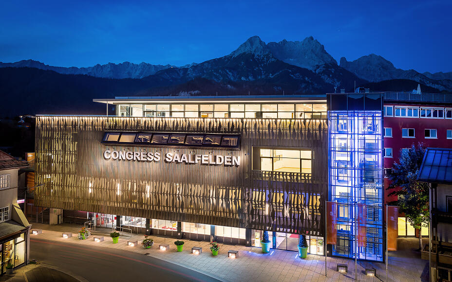 Modernes Congressgebäude in Saalfelden bei Nacht, mit beleuchteter Glasfassade und imposanten Bergkulissen im Hintergrund.