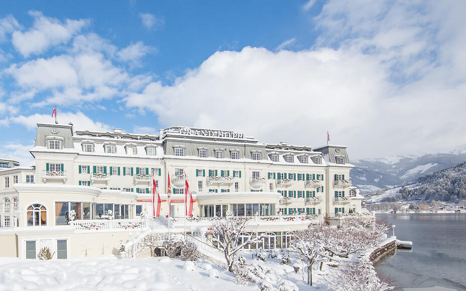 Elegantes Grand Hotel direkt am verschneiten Seeufer mit Blick auf winterliche Berglandschaft und klarem Himmel.