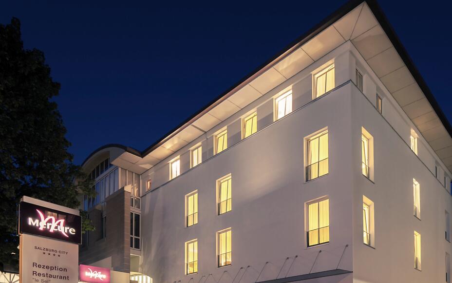Die moderne Fassade des Mercure Salzburg City erstrahlt im warmen Licht. Klare Linien, helle Fenster und die ruhige Abendstimmung schaffen eine einladende Atmosphäre mitten in der Stadt.