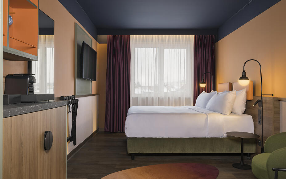 Modern hotel room at Mayburg Salzburg with elegant design, white bed, dark green accents, and warm lighting.