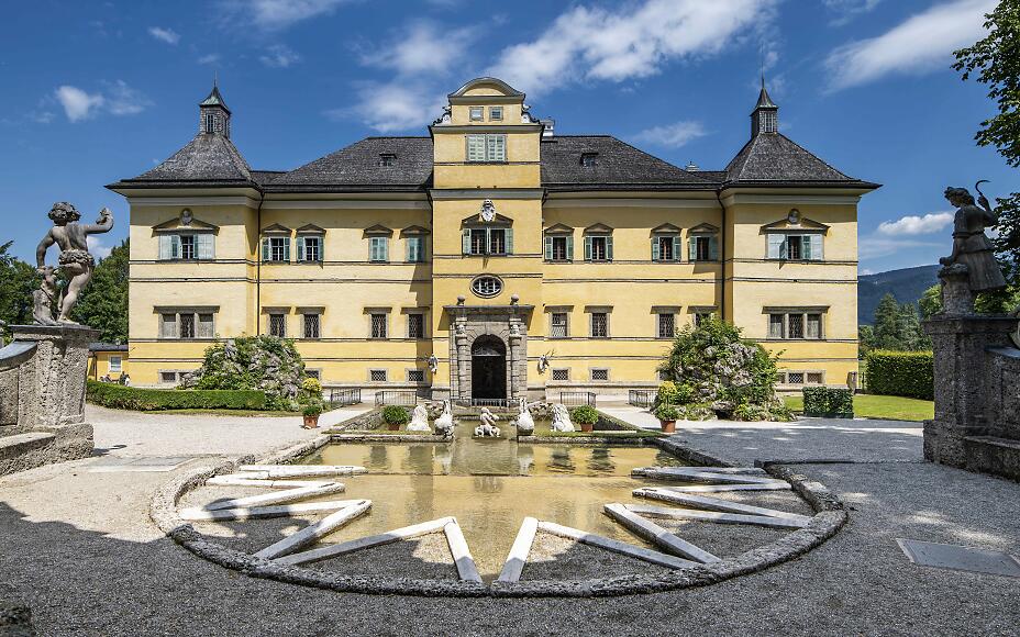 Schloss Hellbrunn, ein barockes Lustschloss vor den Toren Salzburgs, begeistert mit seiner sonnengelben Fassade, kunstvollen Wasserspielen und prachtvoller Gartenanlage. Der Teich mit Skulpturen im Vordergrund verleiht dem Ensemble einen märchenhaften Charakter.