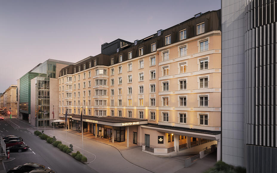 Das Sheraton Grand Salzburg erstrahlt in der Abenddämmerung mit eleganter Fassade, klassischer Architektur und direkter Lage im Herzen der Stadt – ein stilvoller Empfang für anspruchsvolle Gäste.