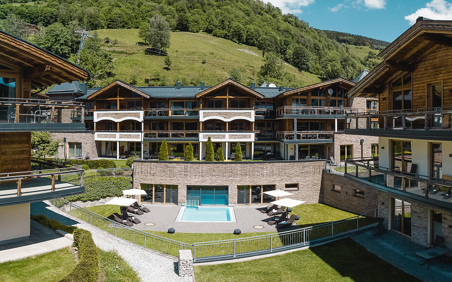 Luxuriöse Chaletanlage mit Swimmingpool im Herzen der Salzburger Berglandschaft, umgeben von sattgrünen Wiesen und bewaldeten Hängen.