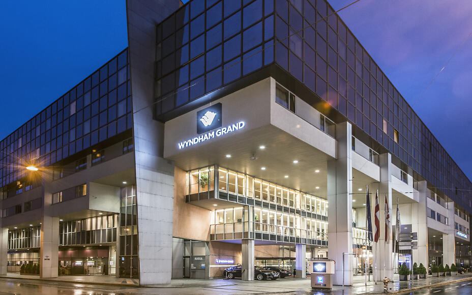 Moderne Hotelarchitektur des Wyndham Grand in Salzburg mit Glasfassade und beleuchteter Eingangshalle in der Abenddämmerung.